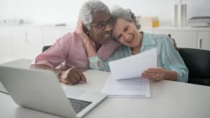 Casal na terceira idade sorrindo em frente ao laptop, simbolizando leveza e confiança no processo de perder o medo da tecnologia e recomeçar com autonomia.