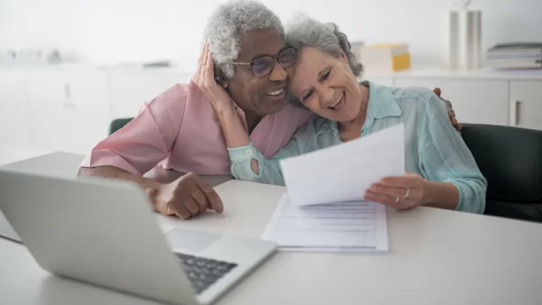 Casal na terceira idade sorrindo em frente ao laptop, simbolizando leveza e confiança no processo de perder o medo da tecnologia e recomeçar com autonomia.