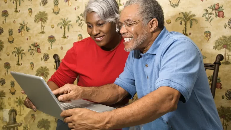 Casal de meia idade sorrindo ao olhar para o laptop, celebrando os primeiros resultados de ganhar dinheiro online com o que já sabem.