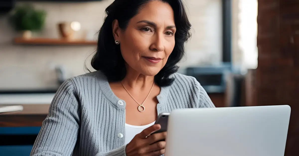 Mulher madura sentada ao computador em casa, representando uma aluna dos cursos online gratuitos para 50+, focada em seu recomeço profissional.
